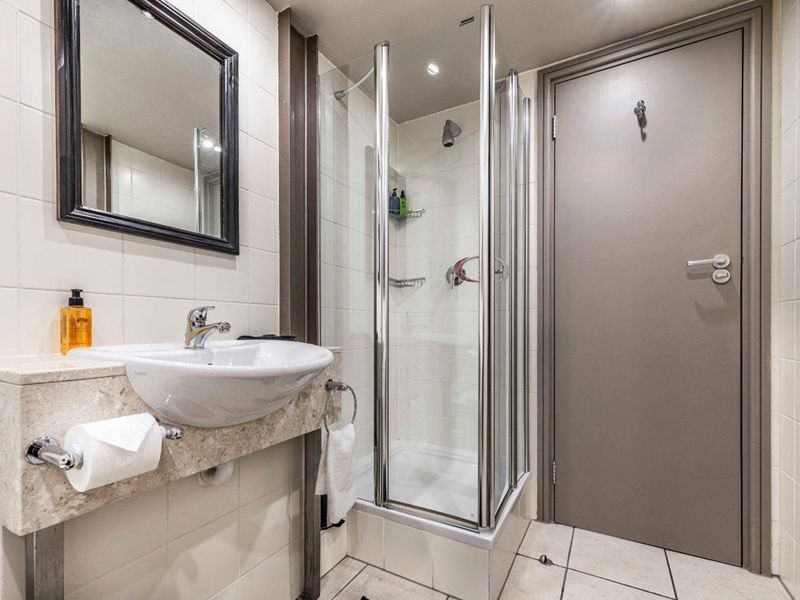 A clean and functional bathroom featuring a modern vanity basin, a glass-enclosed shower, and neutral wall and floor tiling.