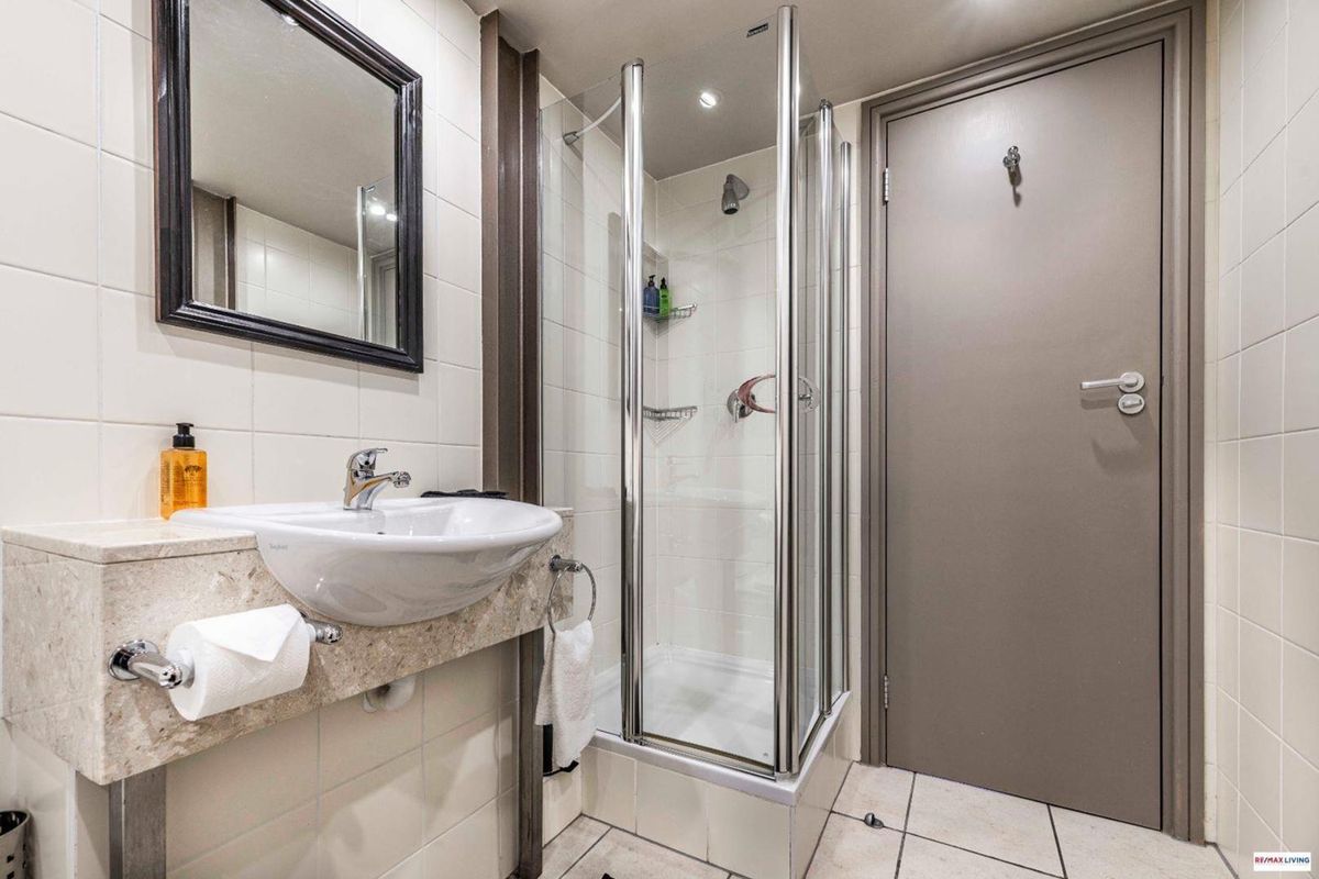 A clean and functional bathroom featuring a modern vanity basin, a glass-enclosed shower, and neutral wall and floor tiling.