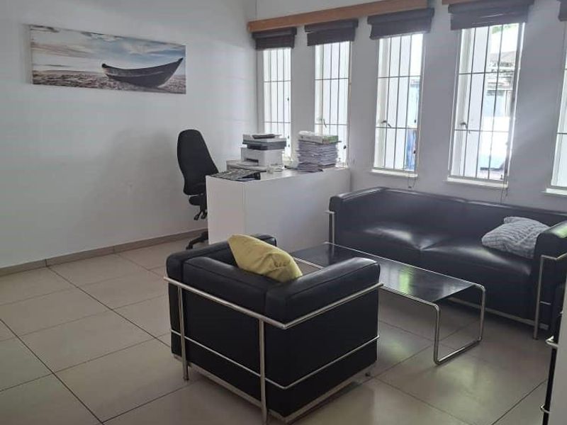 A functional office space featuring tiled flooring, large windows with security bars, and integrated ceiling lighting.
