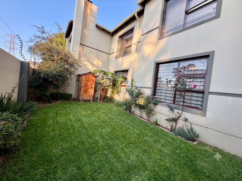 A private rear garden featuring a well-maintained lawn, established landscaping, and a chimney stack with visible exterior wall staining.