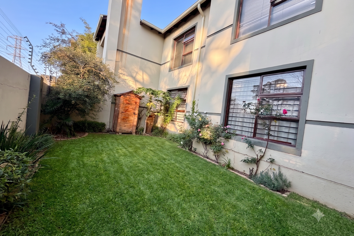 A private rear garden featuring a well-maintained lawn, established landscaping, and a chimney stack with visible exterior wall staining.