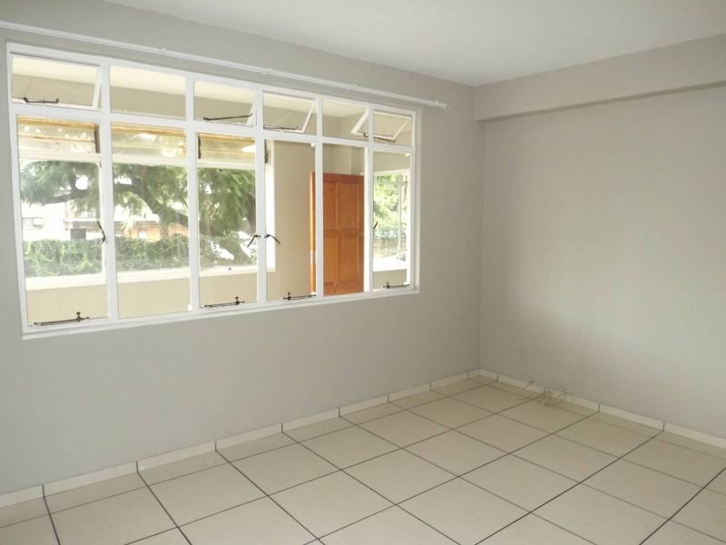 A bright, empty living room featuring neutral tiled flooring and a large multi-pane window providing natural light.