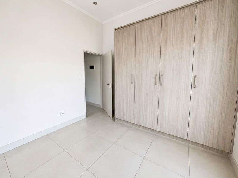 A bright, empty bedroom featuring neutral tiled flooring, modern recessed lighting, and extensive built-in wooden cupboards providing ample storage space.