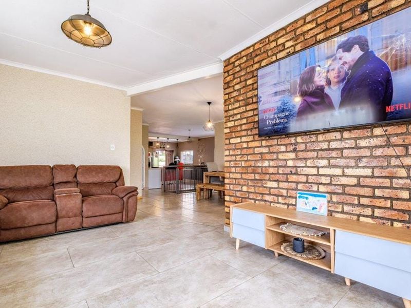 Spacious open-plan living area featuring a prominent exposed brick wall, neutral tiled flooring, and modern pendant lighting, creating a warm and inviting atmosphere.