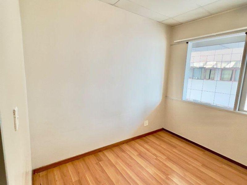 An empty bedroom featuring laminate flooring, a drop ceiling, and a window, providing a blank canvas for personalization.