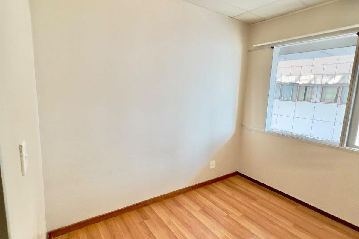 An empty bedroom featuring laminate flooring, a drop ceiling, and a window, providing a blank canvas for personalization.