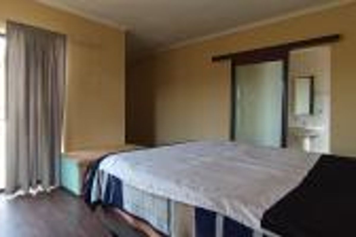 Spacious bedroom featuring laminate flooring, sliding door access to a balcony, and an en-suite bathroom with a pedestal basin.