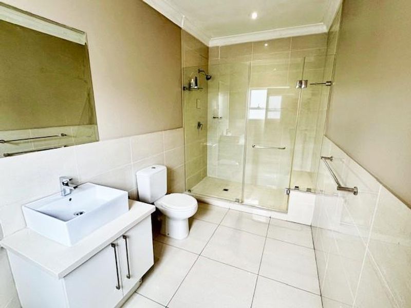 Modern bathroom featuring a white vanity with vessel sink, a glass-enclosed shower, and neutral floor-to-ceiling tiling.