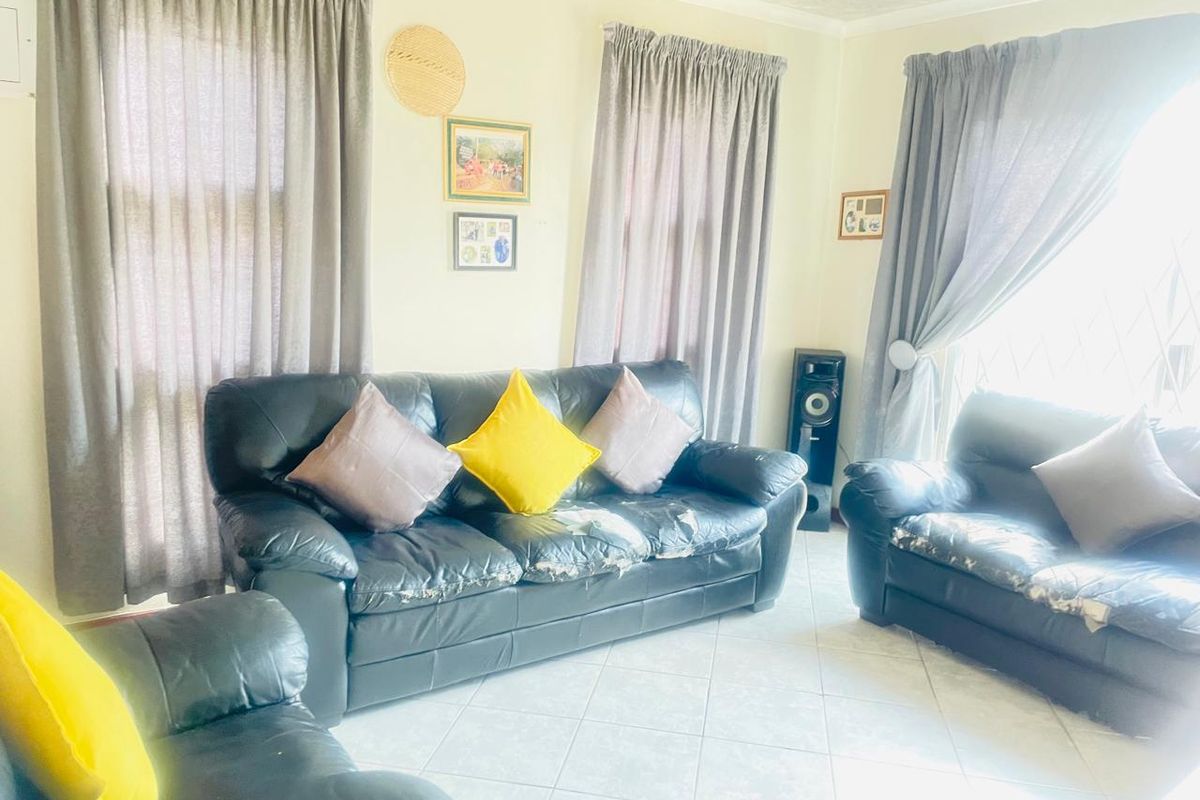 A bright living room featuring tiled flooring and large windows with curtains, providing a functional and well-lit space for relaxation.