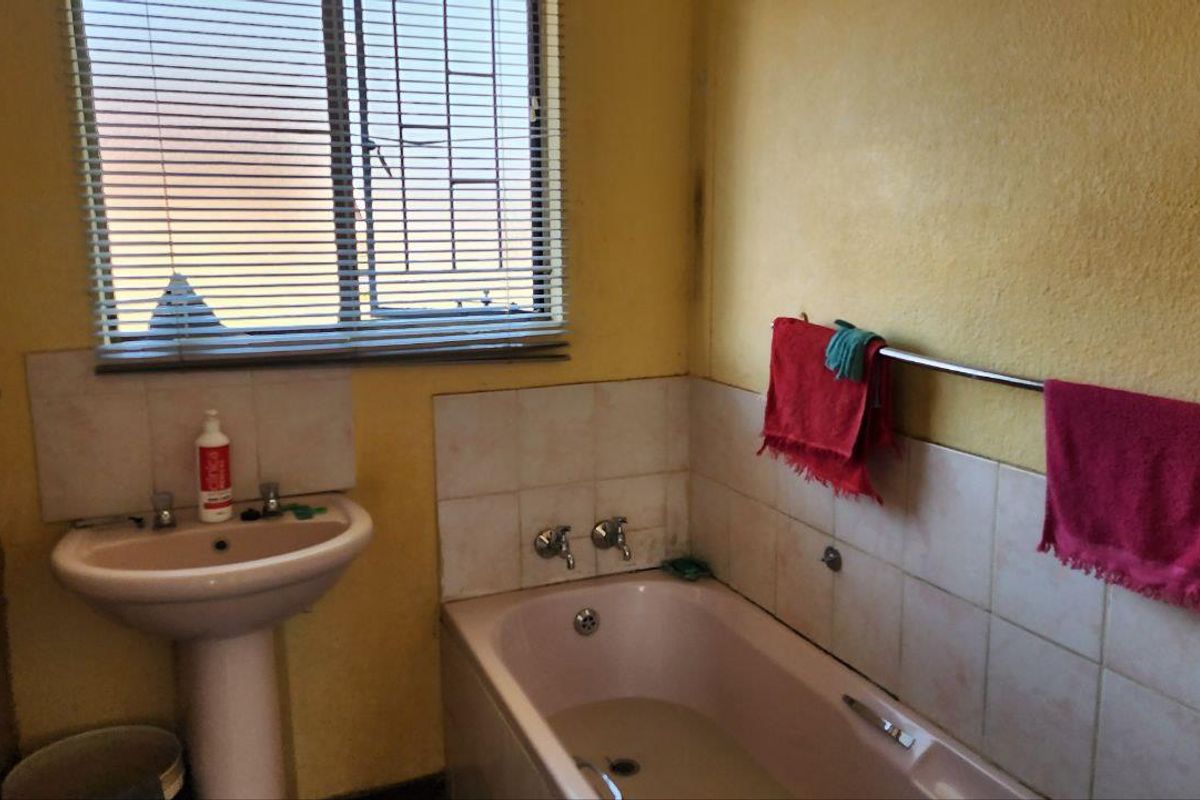 A dated bathroom featuring a pink pedestal basin and matching bathtub, with tiled splashbacks and yellow wall finishes requiring maintenance and cosmetic updates.