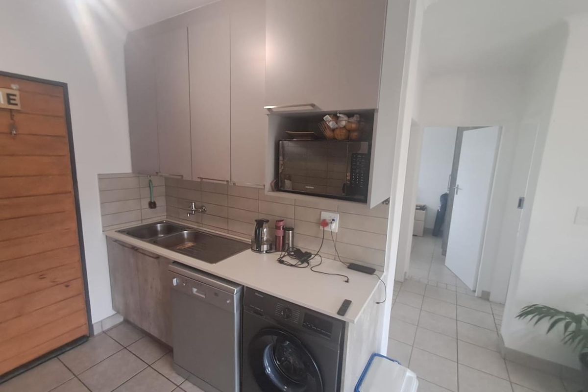 Compact kitchen area featuring modern cabinetry, a stainless steel double sink, tiled backsplash, and dedicated space for under-counter appliances.