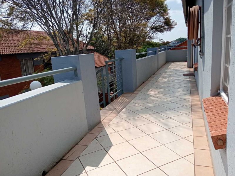 A spacious outdoor balcony featuring tiled flooring, a metal balustrade, and a masonry parapet wall, offering an open-air space for relaxation.