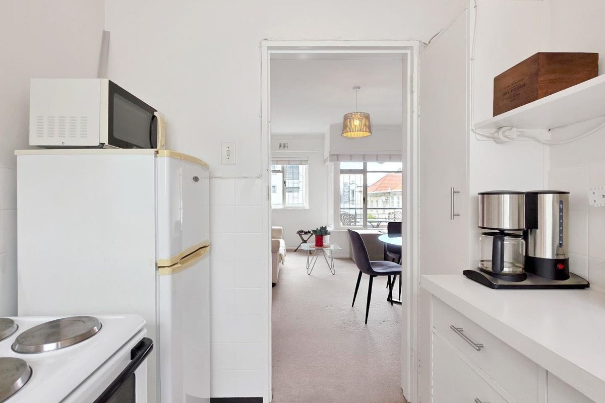 A functional kitchen featuring white cabinetry, tiled splashbacks, and an electric stove, with a direct view into the adjacent living and dining area.