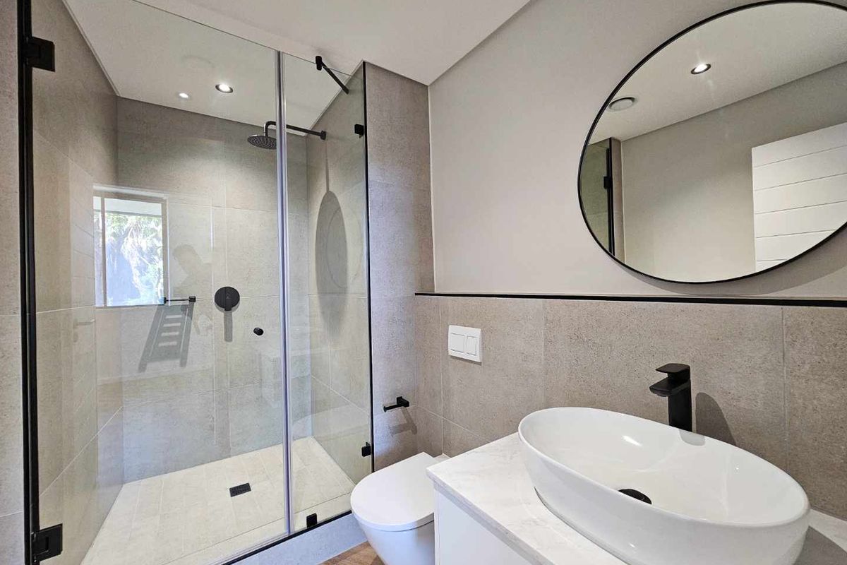 Modern bathroom featuring a glass-enclosed walk-in shower, wall-mounted toilet, and a contemporary vessel sink vanity with matte black fixtures.