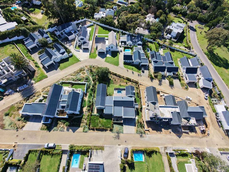 An aerial view of a modern residential estate featuring multiple detached houses with pitched roofs, landscaped gardens, and private swimming pools.