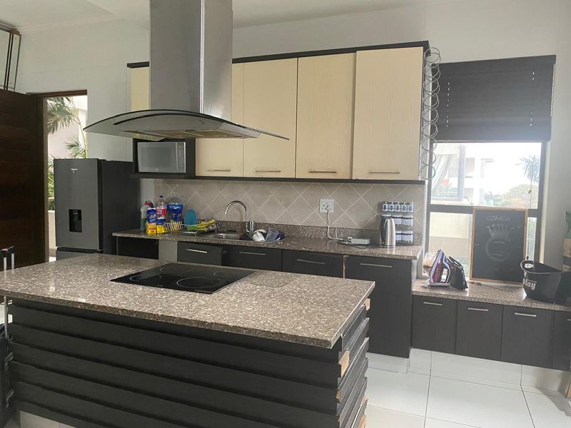 Modern kitchen featuring a central island with an electric cooktop, stone countertops, built-in cabinetry, and a stainless steel extractor fan.