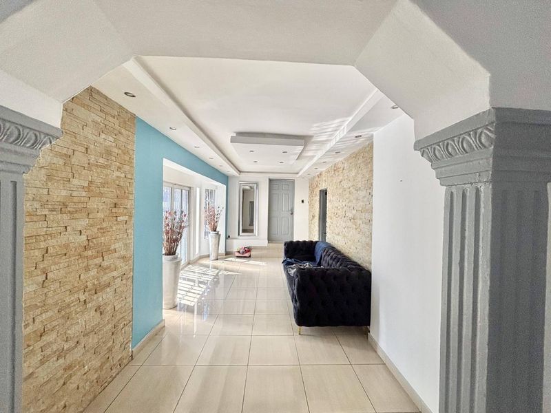 Spacious hallway featuring decorative columns, stone veneer wall accents, tiled flooring, and a coffered ceiling with recessed lighting.