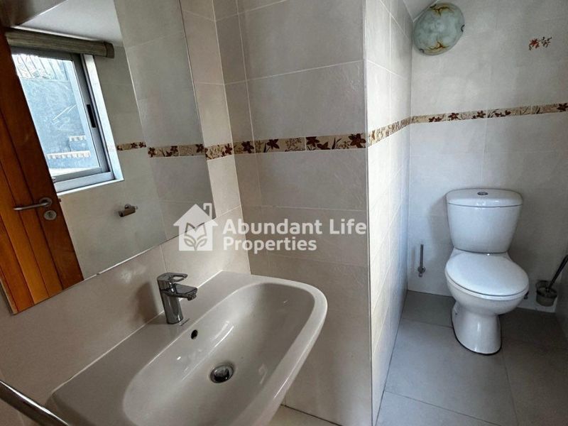 A functional bathroom featuring tiled walls and flooring, a wall-mounted basin with a chrome mixer tap, and a standard toilet.