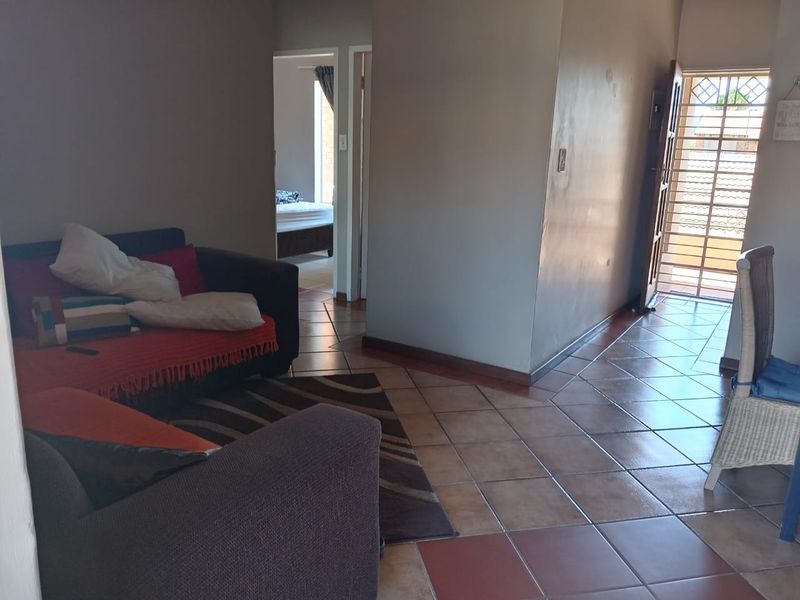 A living area featuring tiled flooring and a security gate at the entrance, with a view leading into an adjacent bedroom.