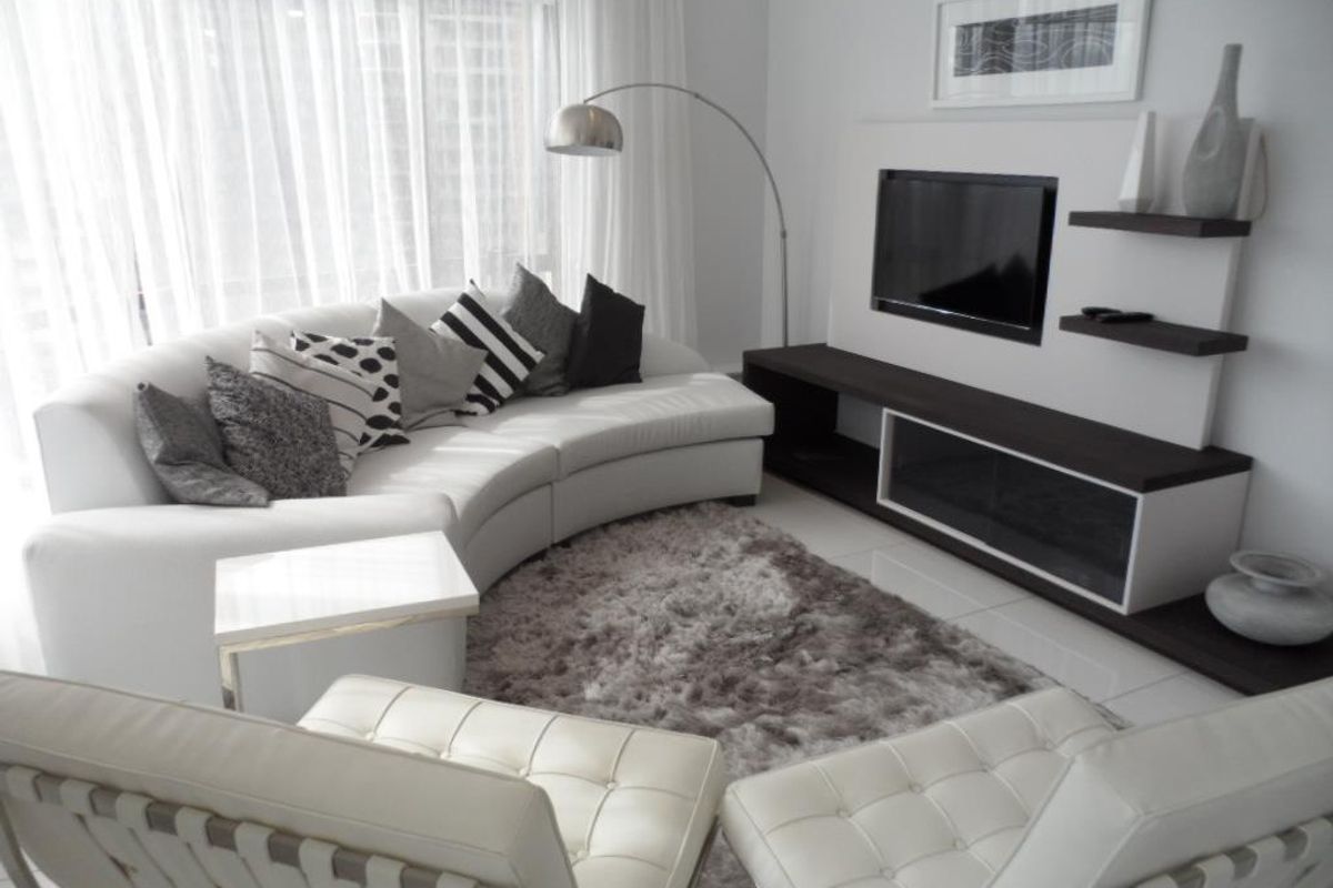 A modern living room featuring a built-in media console with integrated shelving and large floor-to-ceiling windows with sheer curtains.