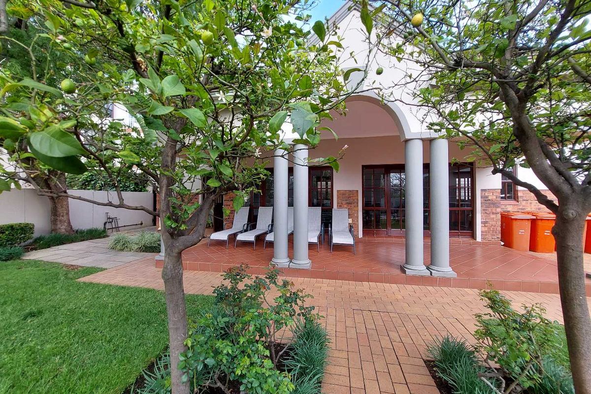 A rear view of the property featuring a covered patio with columns, brick paving, and access through sliding doors to the garden area.