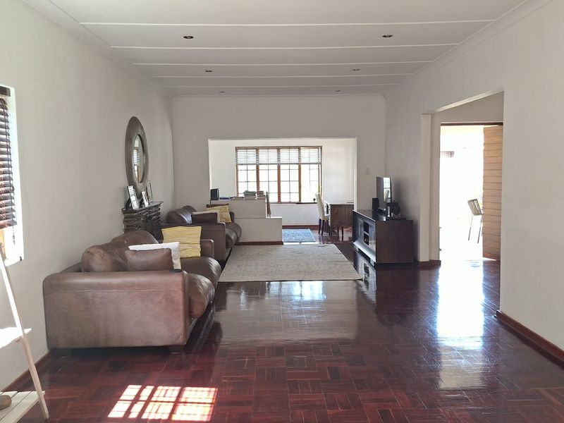 Spacious open-plan living area featuring polished parquet flooring, recessed lighting, and large windows with wooden frames, offering a bright and versatile layout.