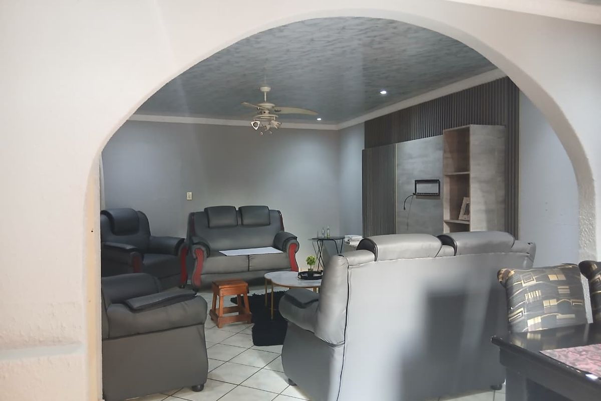 A living room featuring a decorative arched entryway, tiled flooring, a ceiling fan, and a modern slatted wood feature wall.