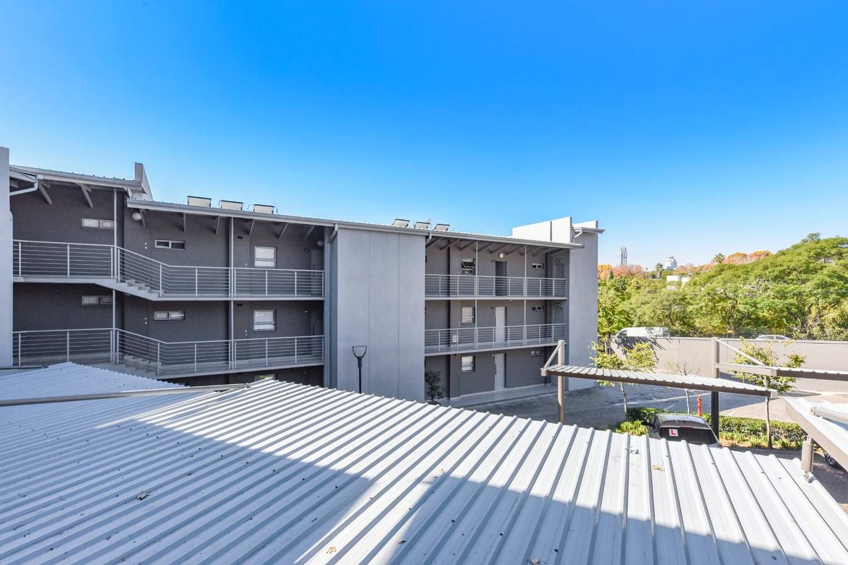Exterior view of a multi-story apartment building featuring metal roofing, open-air walkways with metal railings, and a clear blue sky.