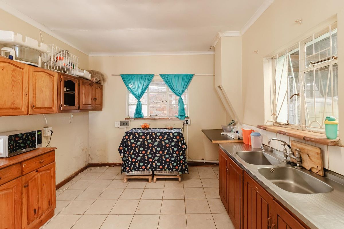 A dated kitchen featuring wooden cabinetry, a double stainless steel sink, and tiled flooring, offering a functional space with potential for modernization.