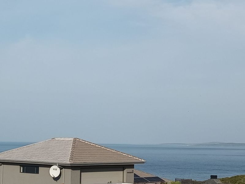 A scenic coastal view overlooking the ocean, featuring a residential roofline with a satellite dish and solar panels in the foreground.