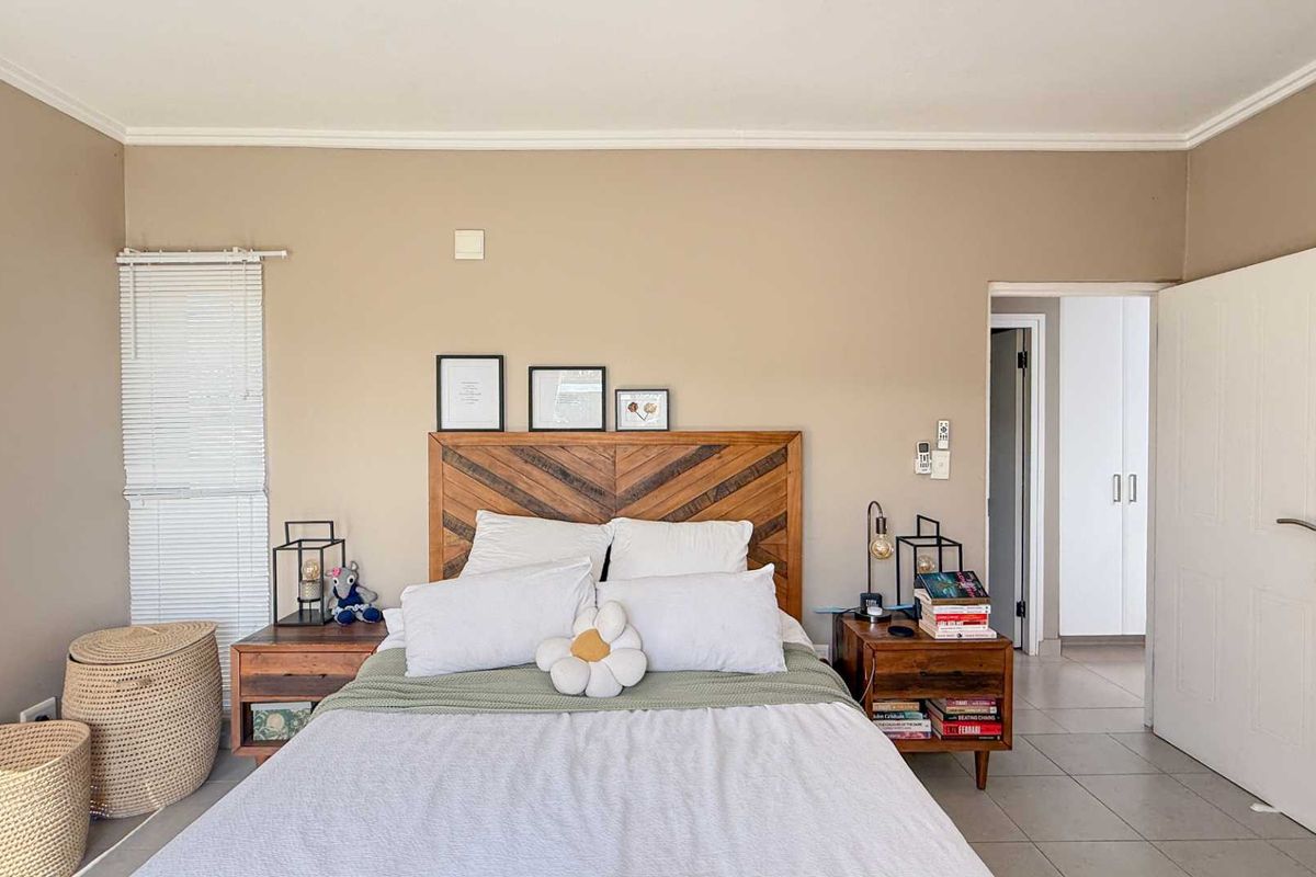 A well-lit bedroom featuring neutral wall tones, tiled flooring, and a doorway leading to a built-in cupboard area.