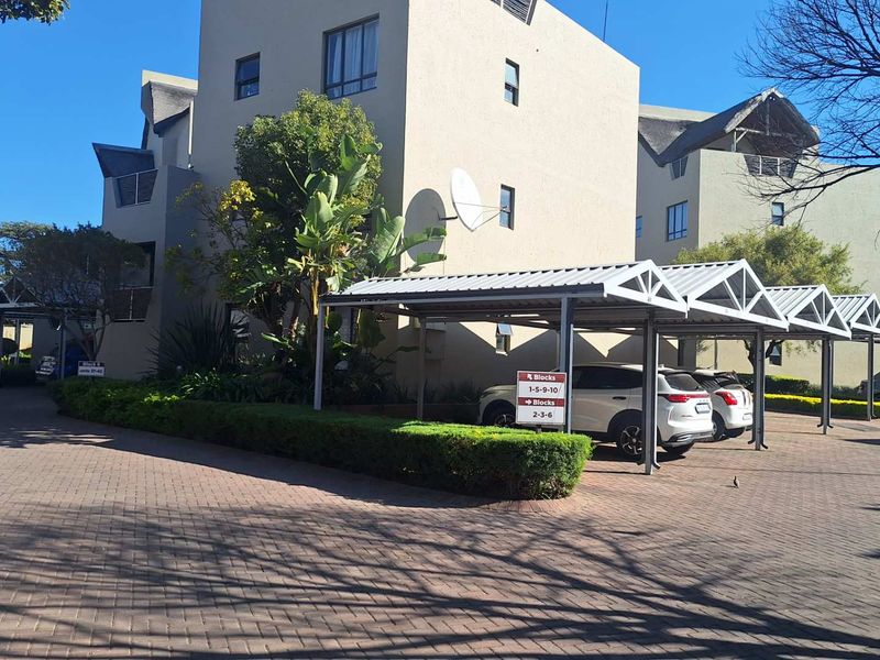 Exterior view of the apartment complex featuring a paved driveway, covered parking carports, and established landscaping.