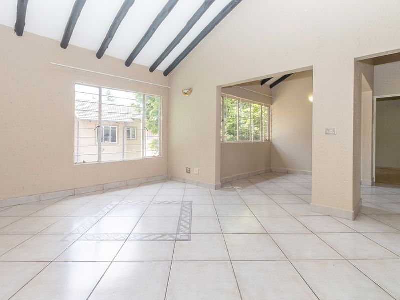 Spacious open-plan living area featuring vaulted ceilings with exposed timber beams, neutral tiled flooring, and large windows providing ample natural light.