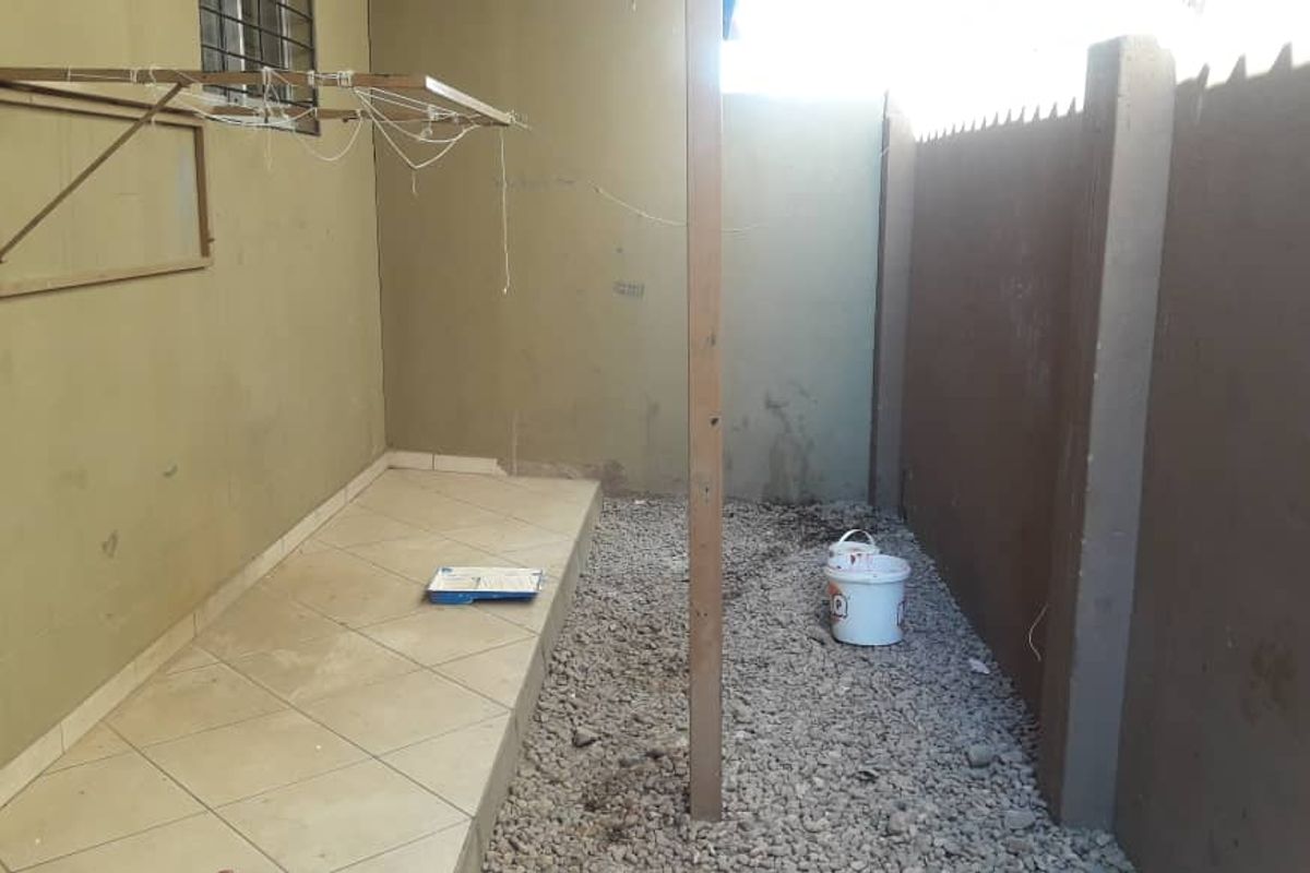 A small outdoor utility area featuring a tiled section, gravel ground, and a wall-mounted drying rack, enclosed by perimeter walls.