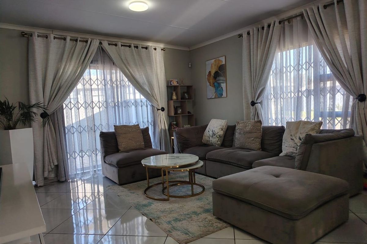 A well-maintained living room featuring large windows with security gates, tiled flooring, and neutral wall tones, providing a bright and comfortable living space.