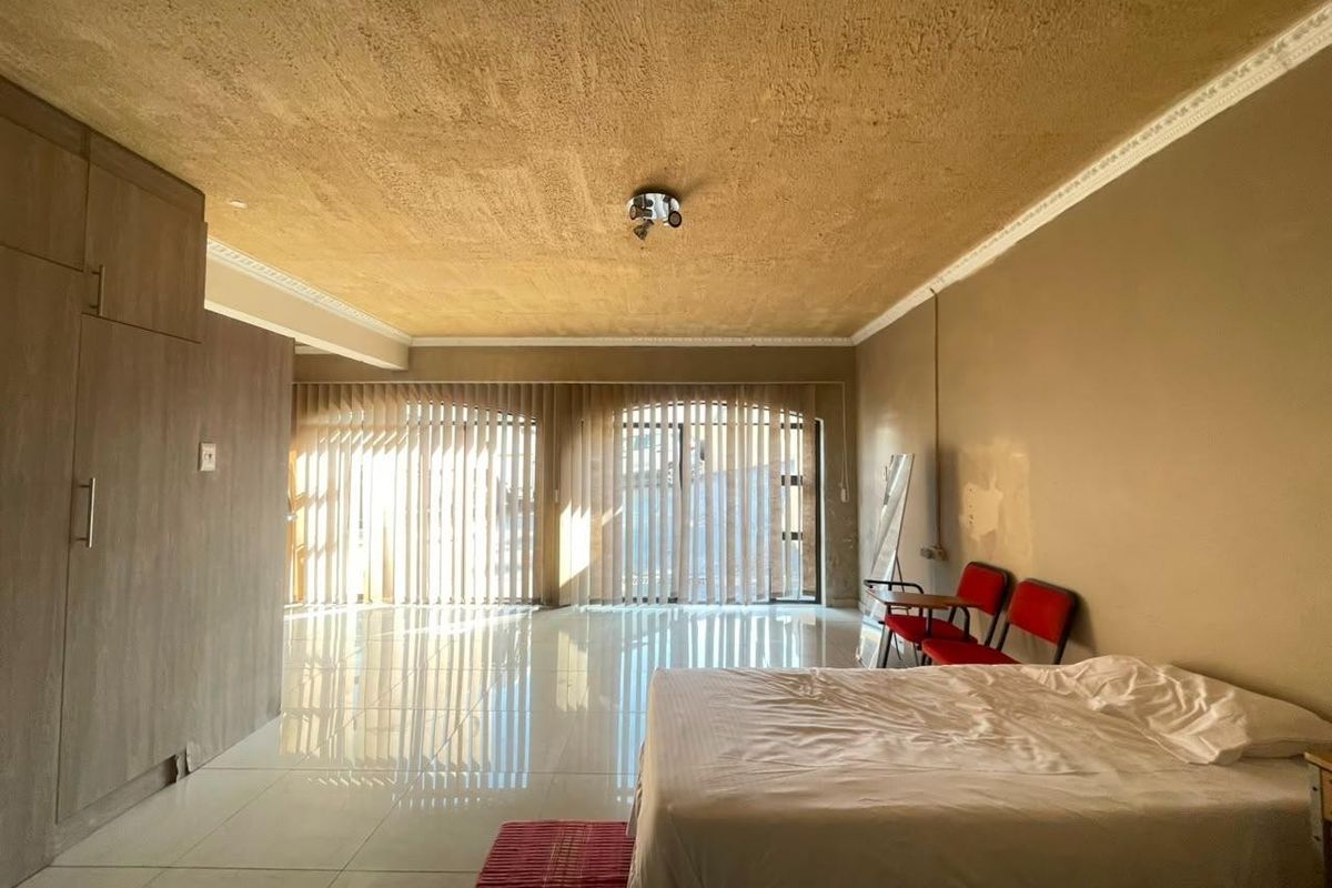 Spacious bedroom featuring large sliding glass doors with vertical blinds, tiled flooring, and built-in cupboards, offering a bright and open living space.