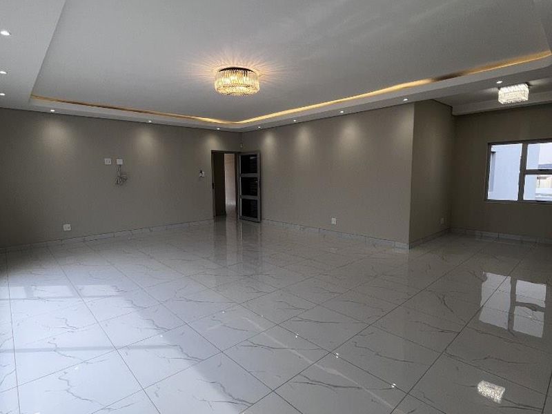 Spacious, modern living area featuring high-gloss marble-look porcelain tiles, recessed tray ceiling with ambient LED lighting, and elegant crystal light fixtures.