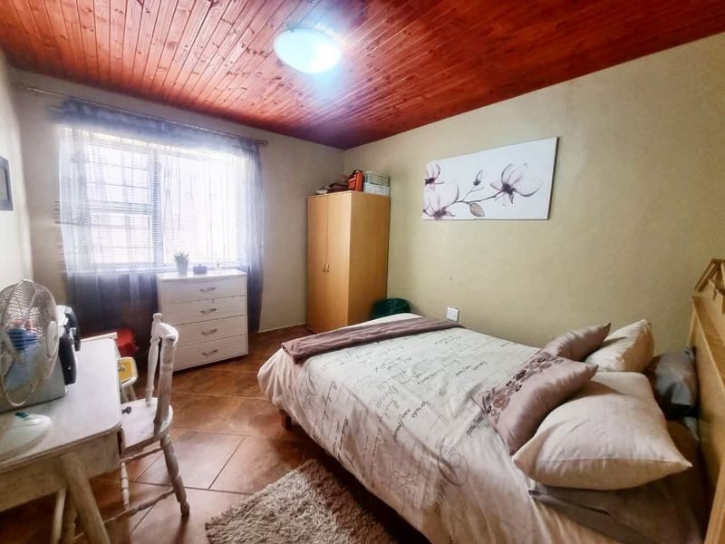 A bedroom featuring a warm timber tongue and groove ceiling, tiled flooring, and a window fitted with security burglar bars.
