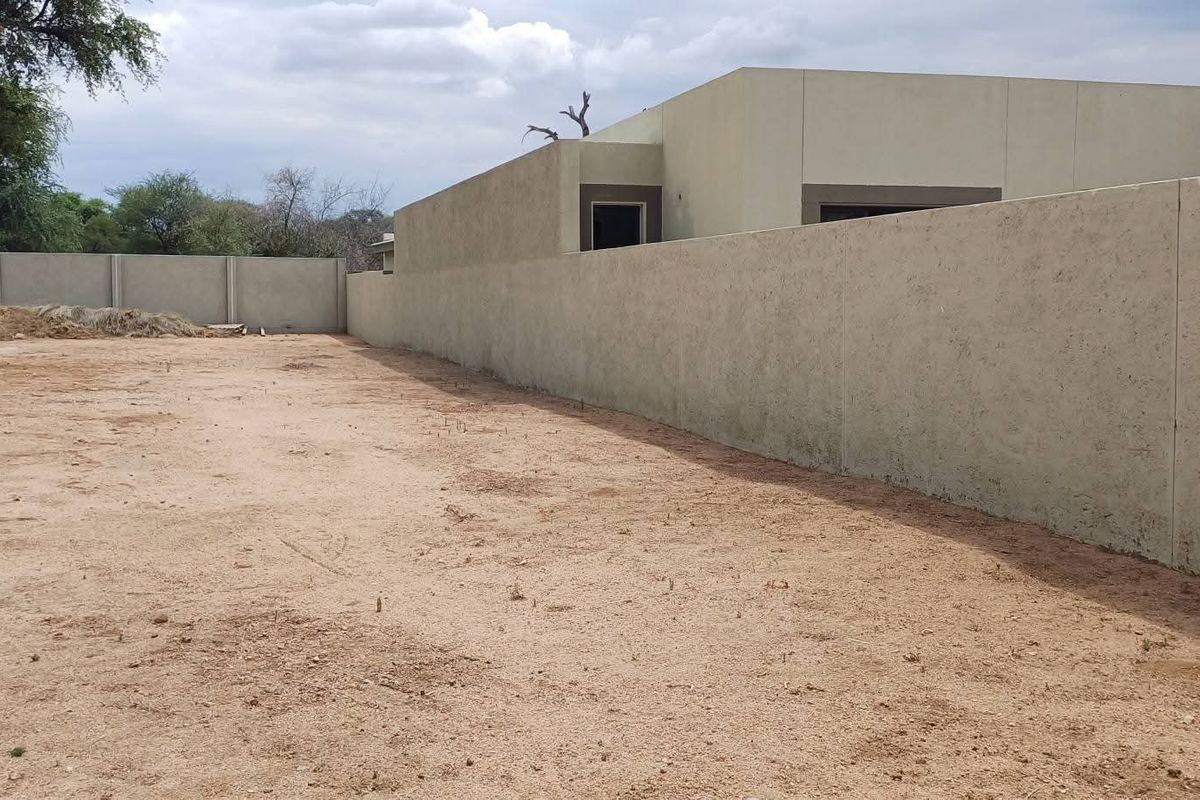 A vacant residential plot featuring a secure precast concrete boundary wall and cleared ground, ready for development.