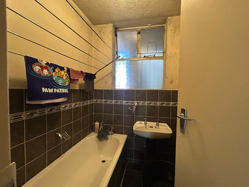 A dated bathroom featuring a bathtub, wall-mounted basin, and tiled splashbacks, currently requiring significant maintenance and cosmetic renovation to address wall and ceiling deterioration.