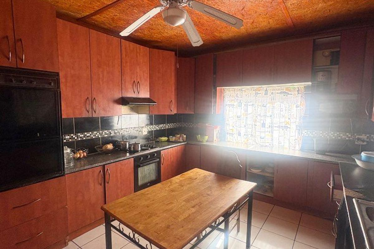 A functional kitchen featuring wood-toned cabinetry, tiled flooring, a built-in oven, and a ceiling fan, offering a practical layout for daily meal preparation.