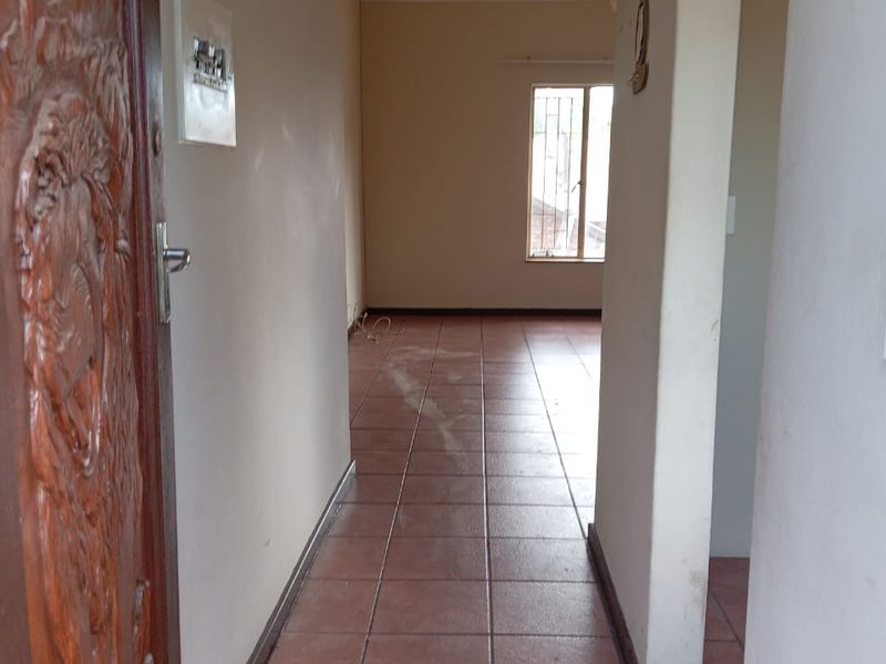 An empty hallway featuring tiled flooring and a decorative carved wooden entrance door, leading into an open living space with natural light.