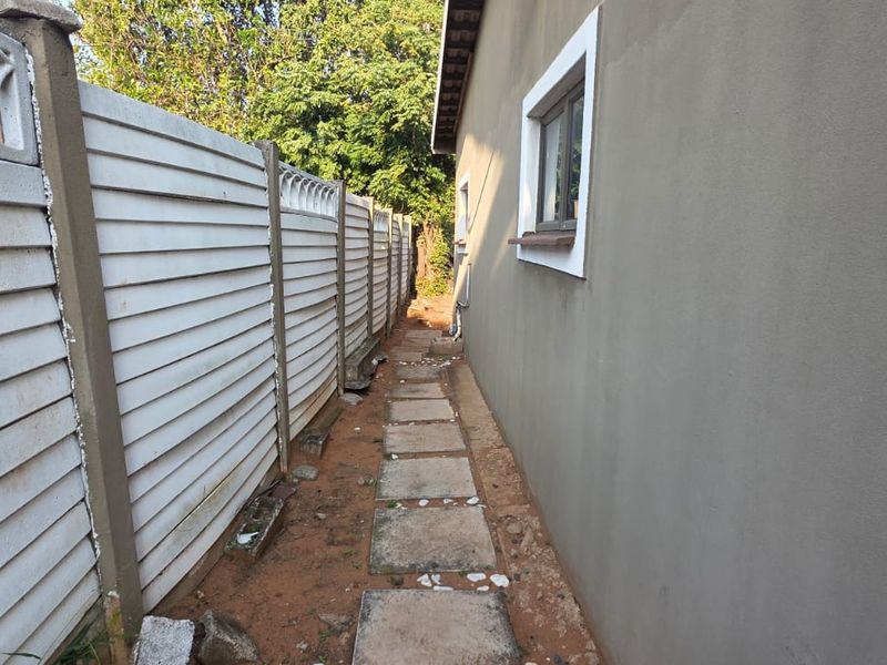 A narrow side passage of the cottage featuring a precast concrete boundary wall, paved walkway, and exterior wall finish.