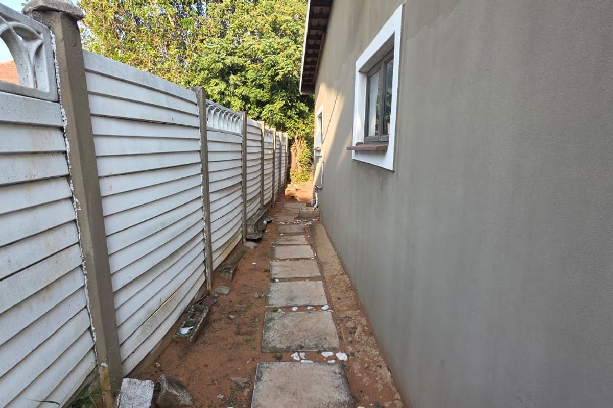 A narrow side passage of the cottage featuring a precast concrete boundary wall, paved walkway, and exterior wall finish.