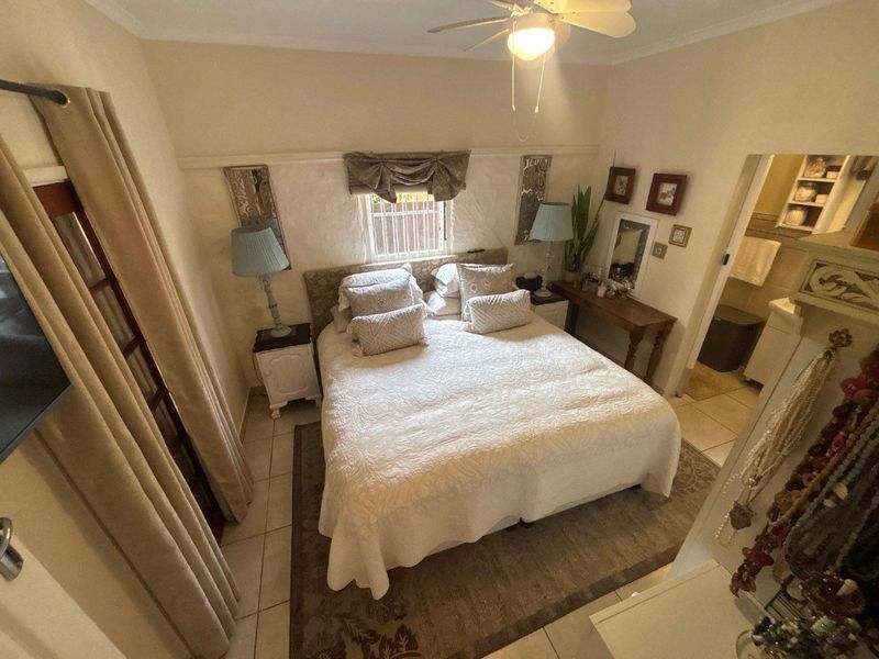 A cozy bedroom featuring tiled flooring, a ceiling fan, and an adjoining en-suite bathroom, providing a functional and comfortable living space.