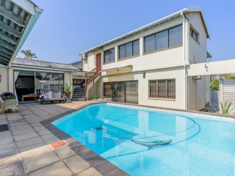 A spacious outdoor pool area featuring a paved patio, external staircase access to the upper level, and sliding glass doors leading into the home.