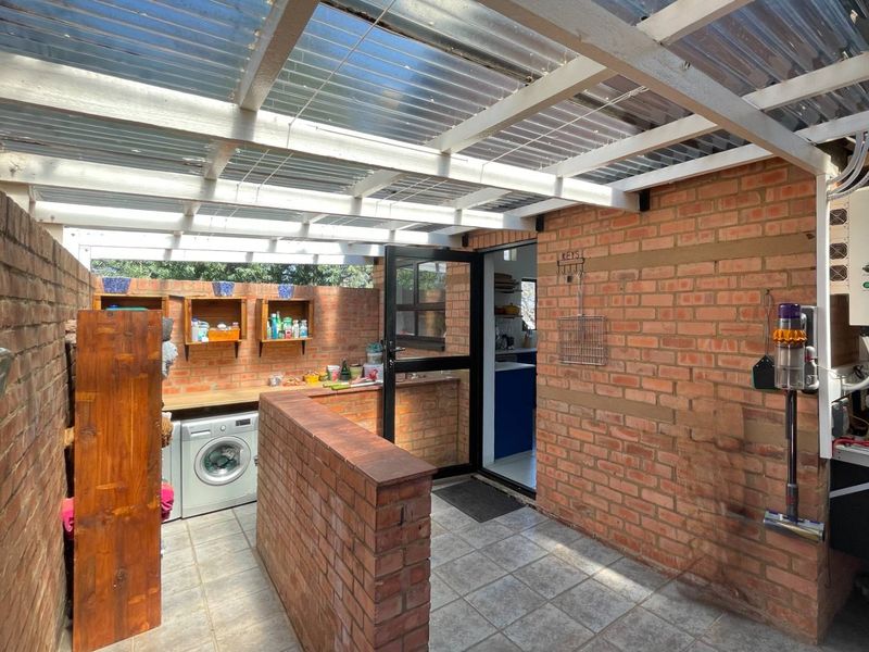 A functional outdoor laundry area featuring exposed brick walls, tiled flooring, and a translucent corrugated roof providing natural light.