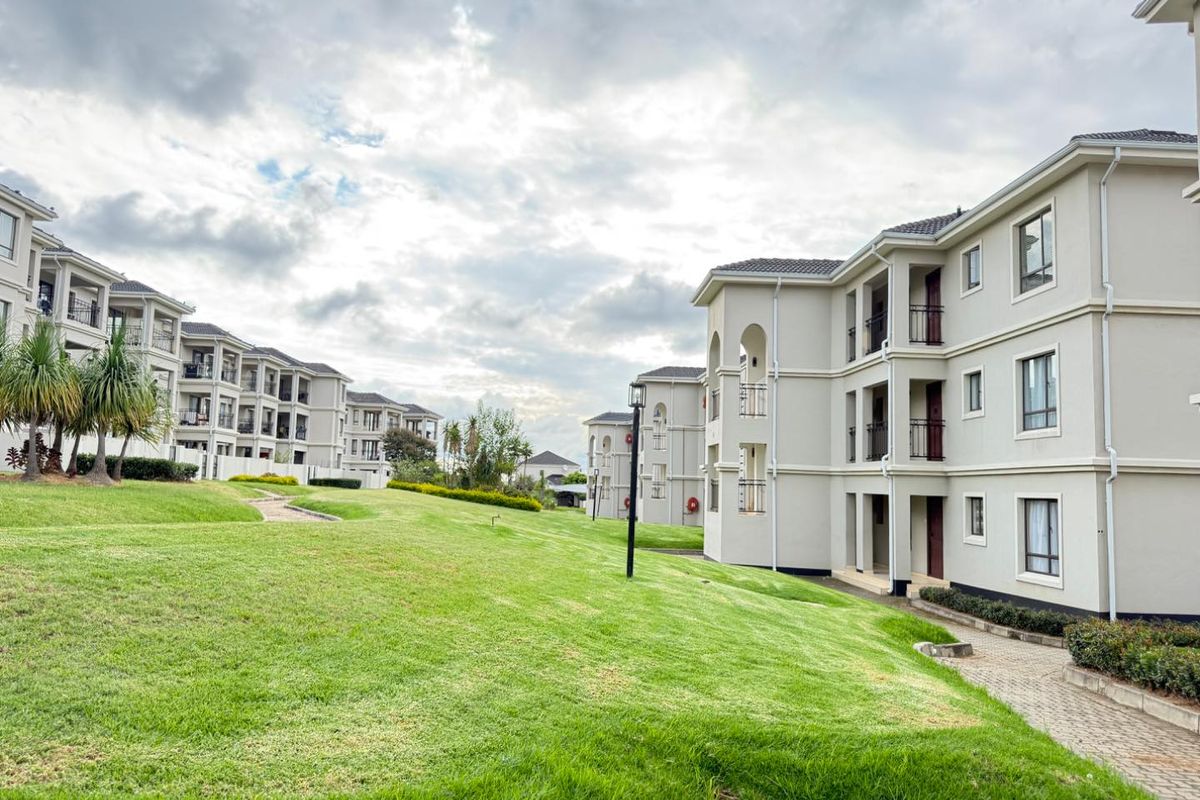 A view of the apartment complex grounds featuring well-maintained lawns, paved pathways, and multi-story residential buildings with balconies.