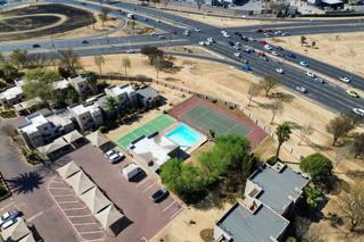 Aerial view of the townhouse complex featuring a swimming pool, tennis court, and covered parking facilities, situated near a major road intersection.