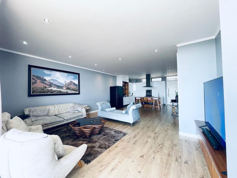 Spacious open-plan living area featuring modern laminate flooring, recessed lighting, and a contemporary kitchen with a central island and high-gloss cabinetry.